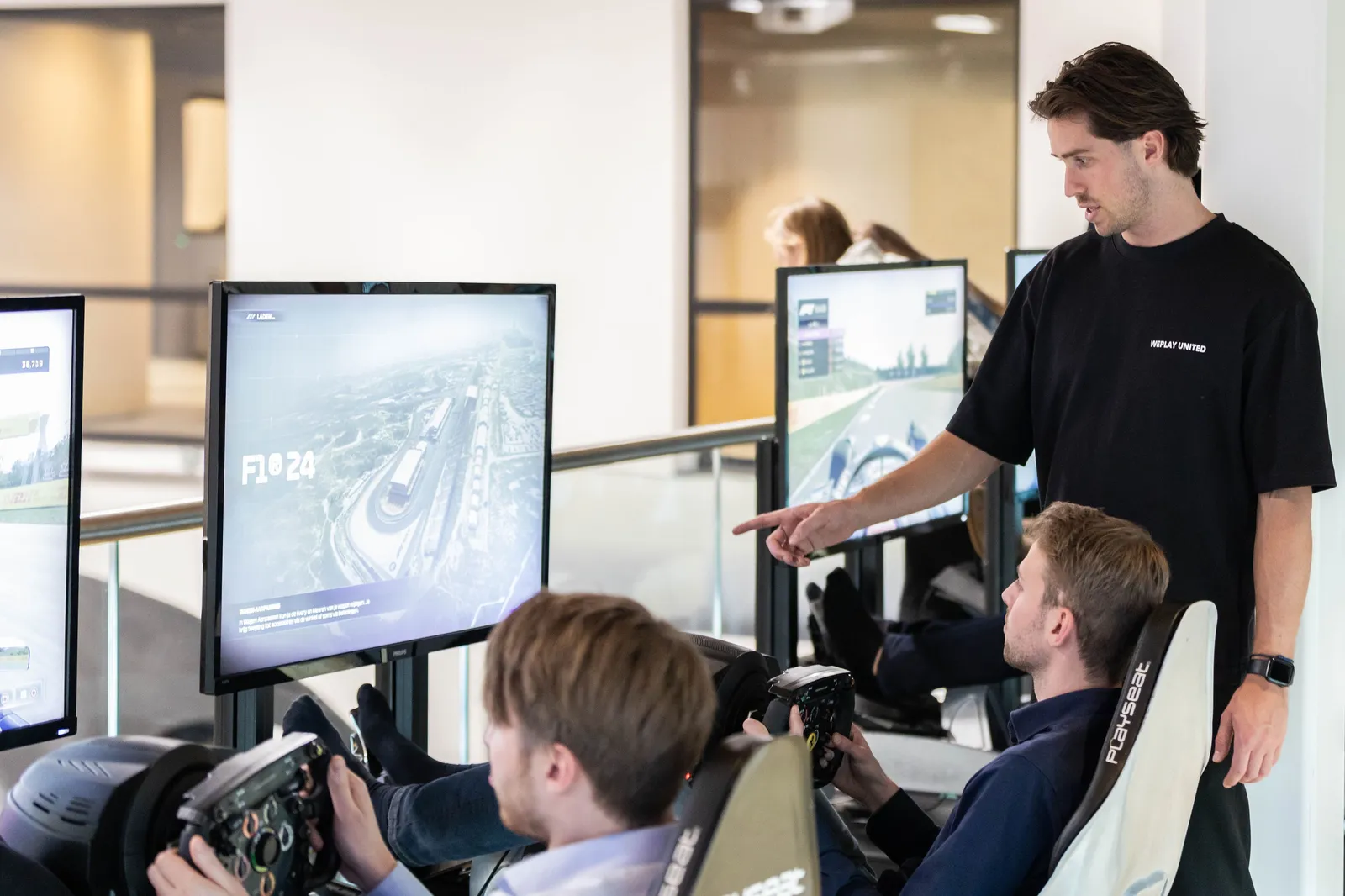 Collega's kijken toe terwijl deelnemers racen in F1-simulatoren tijdens een bedrijfsevent van WePlay United