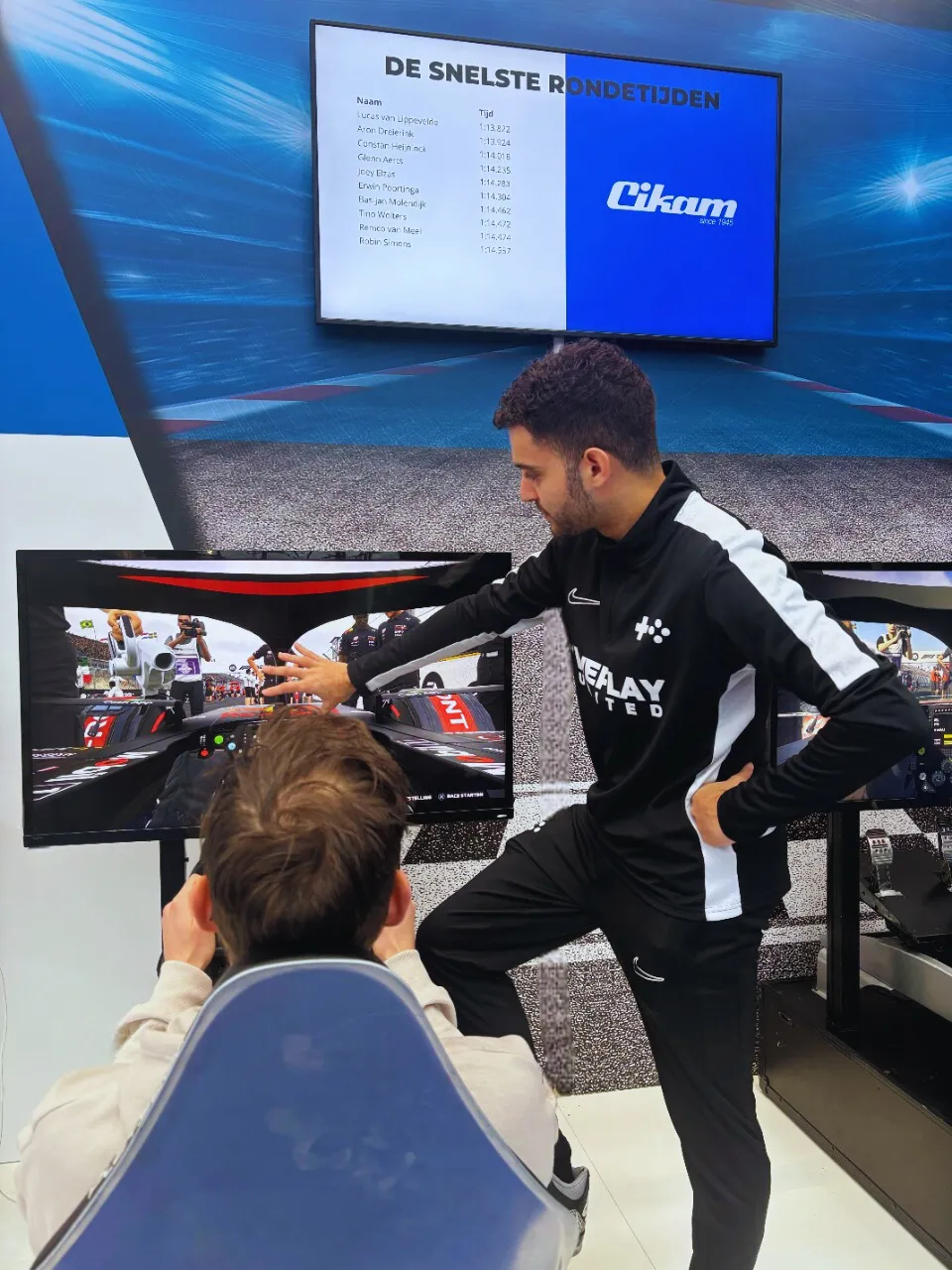 Eventmanager van WePlay United begeleidt een deelnemer bij een F1-simulator op een beursstand