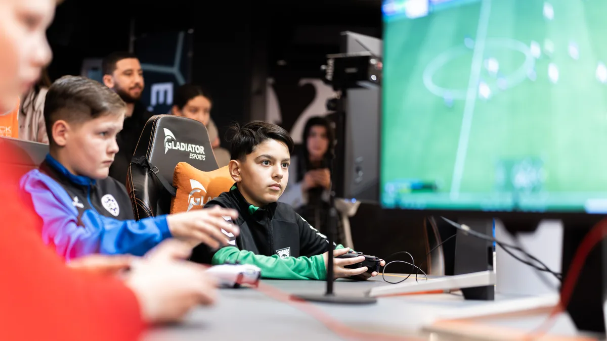 Jongen speelt geconcentreerd EA FC met controller terwijl de gameplay zichtbaar is op het scherm