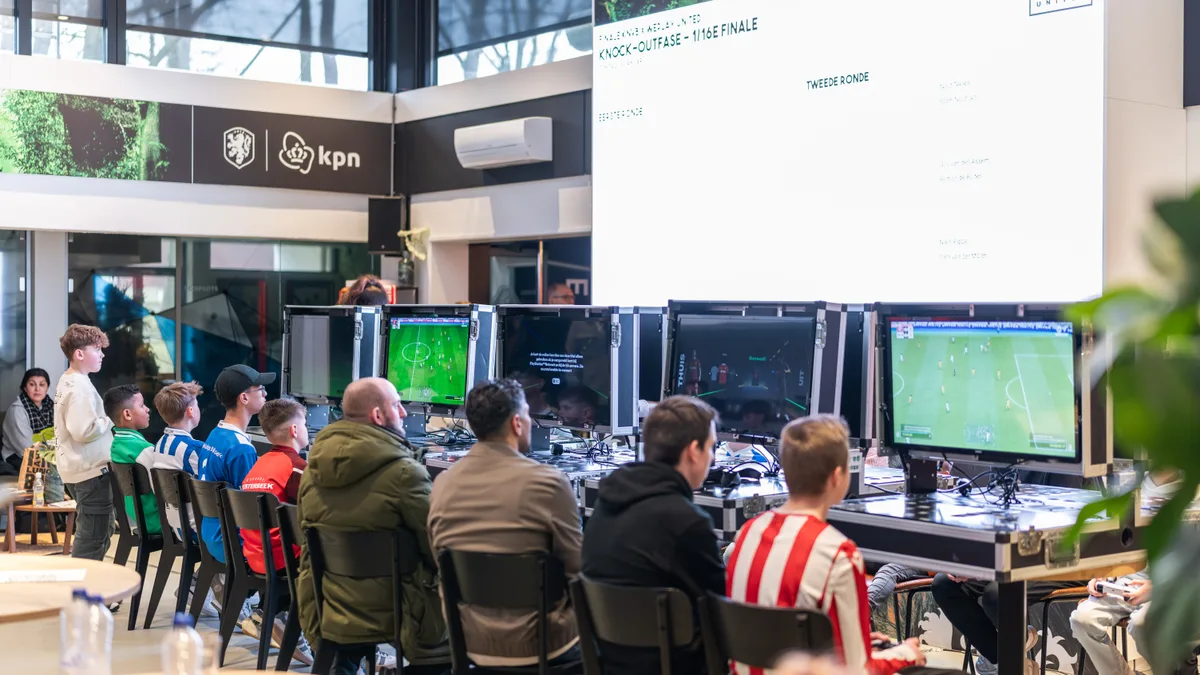 Drukbezochte KPN E_Room tijdens de knock-outfase met gamestations en toernooischema op groot scherm