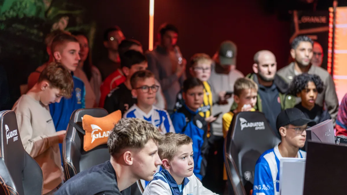 Grote groep kinderen in voetbalshirts kijkt naar de finalewedstrijd in de esports room
