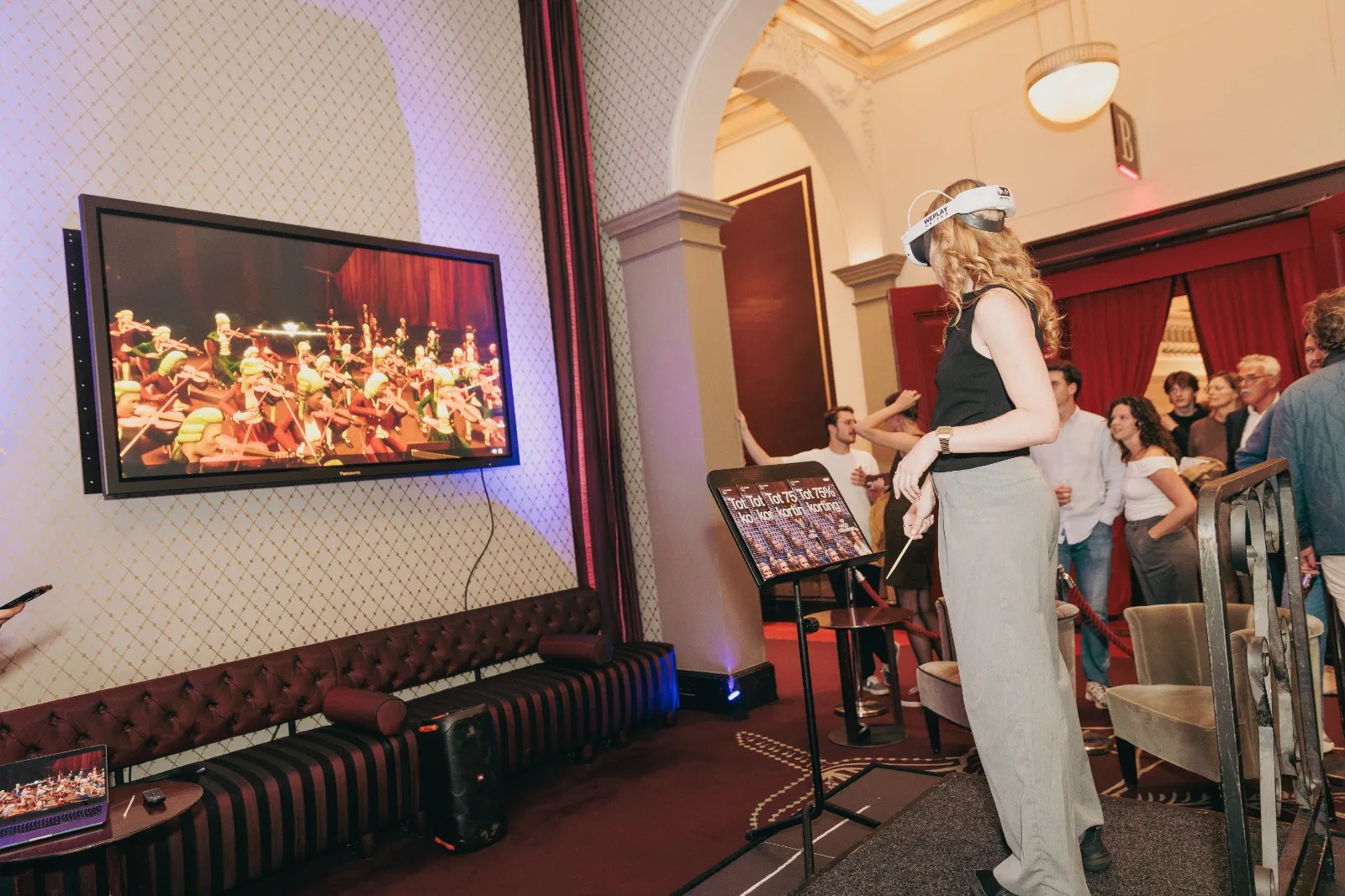 Bezoeker met VR-bril dirigeert een virtueel orkest in de VR-game Maestro in het Concertgebouw Amsterdam, publiek kijkt mee