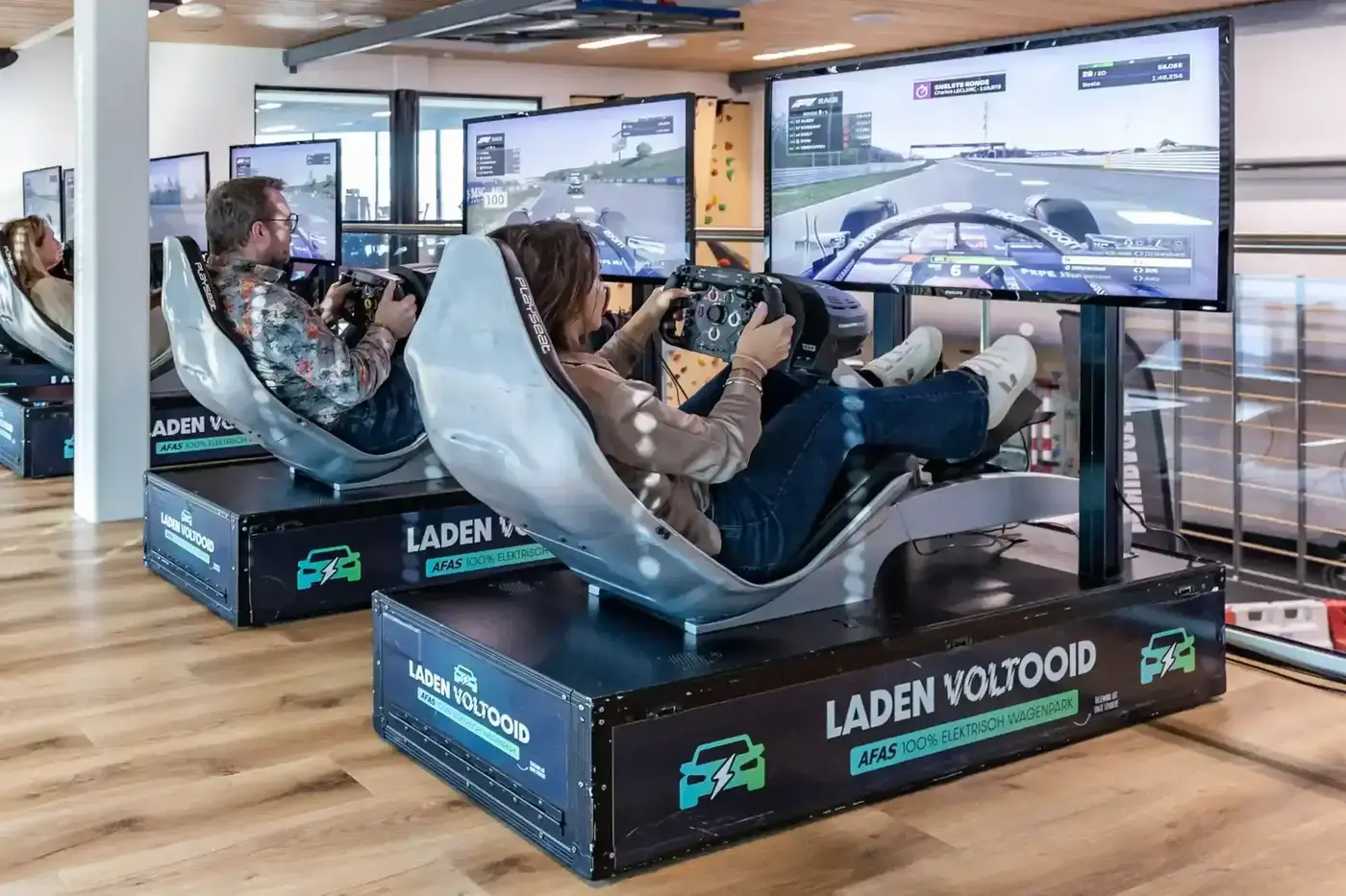 Deelnemers racen naast elkaar in F1-simulatoren met Playseat-stoelen en grote schermen op een bedrijfsevenement