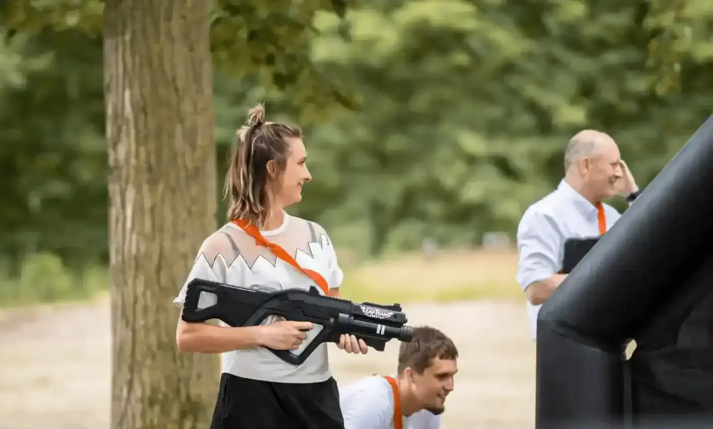 Jonge vrouw met laserwapen speelt lasergamen in een bosrijke omgeving met opblaasbare obstakels