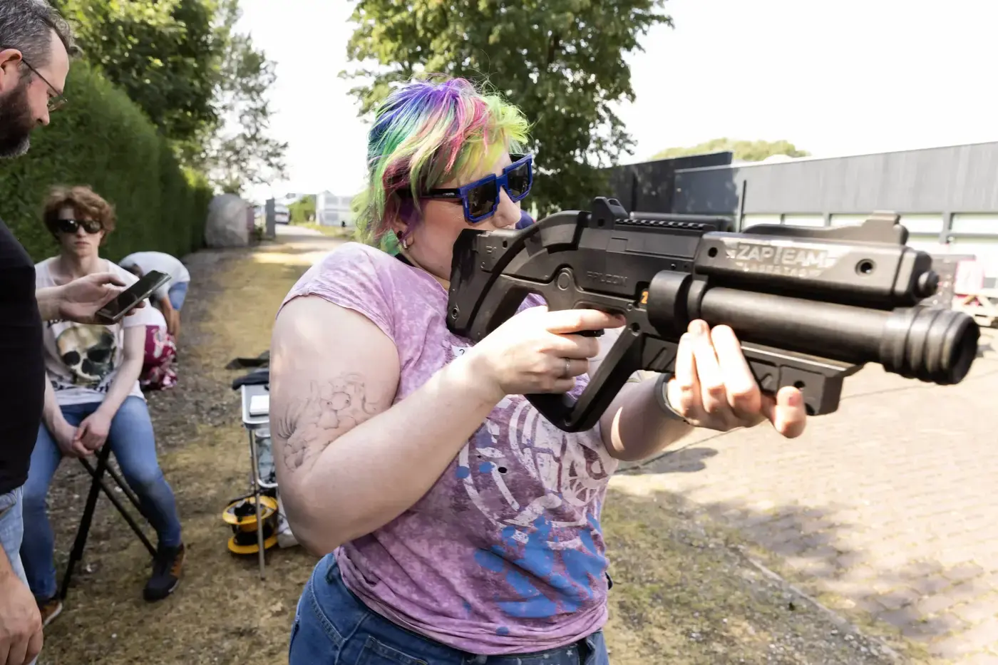 Vrouw met kleurrijk haar richt lachend een professioneel lasergame-wapen tijdens een buitenevenement