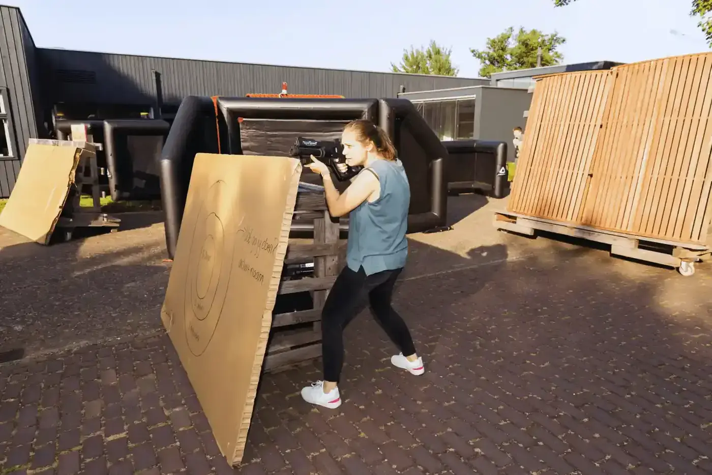 Vrouw schiet met laserpistool vanachter dekking tijdens een lasergame event op een bedrijventerrein