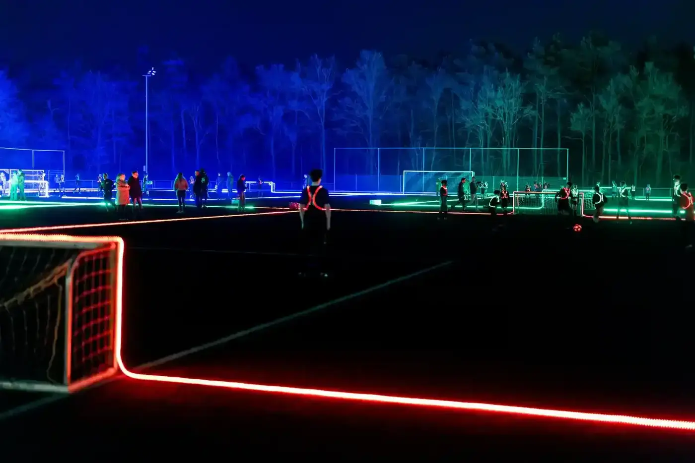 Spelers op een LED-voetbalveld bij nacht met oplichtende doelen en neon belijning in rood en groen