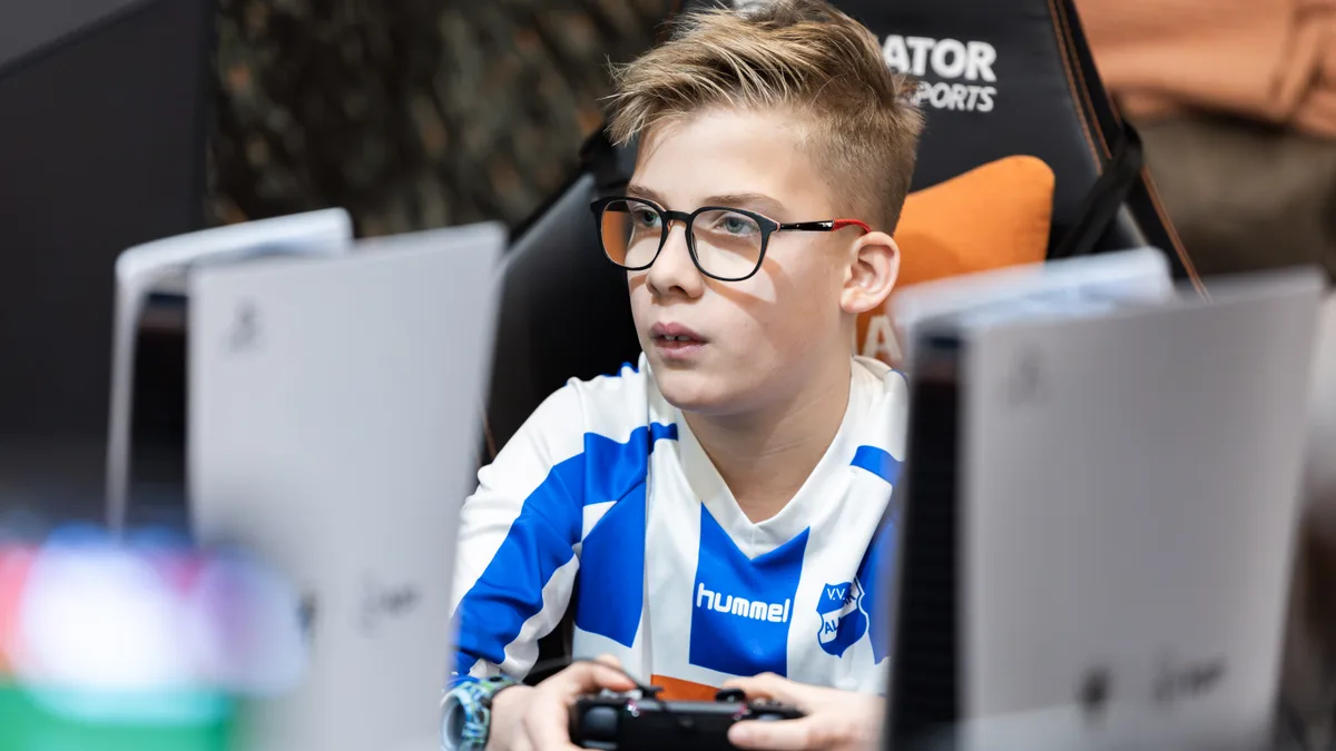 Geconcentreerde jongen in voetbalshirt speelt EA FC met PS5-controller in Gladiator gaming stoel