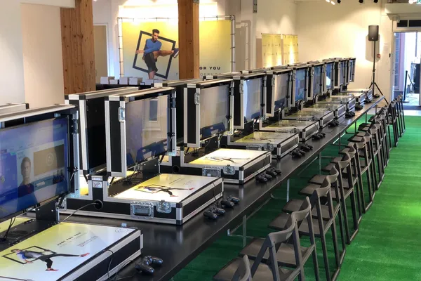 Rij professionele gaming stations met schermen in flightcases opgesteld in een winkelcentrum