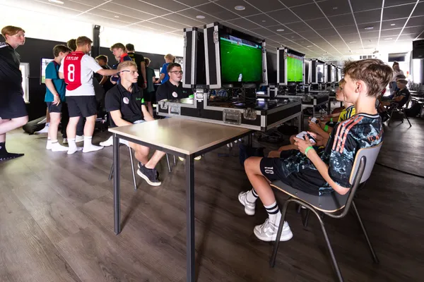 Jongeren in voetbalshirts spelen FIFA op gaming stations tijdens KNVB finaledag